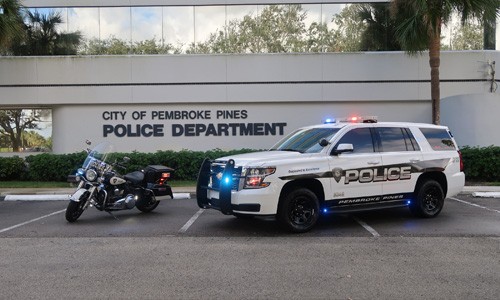 A police car and motorcycle parked in front of the city of pembroke pines department.